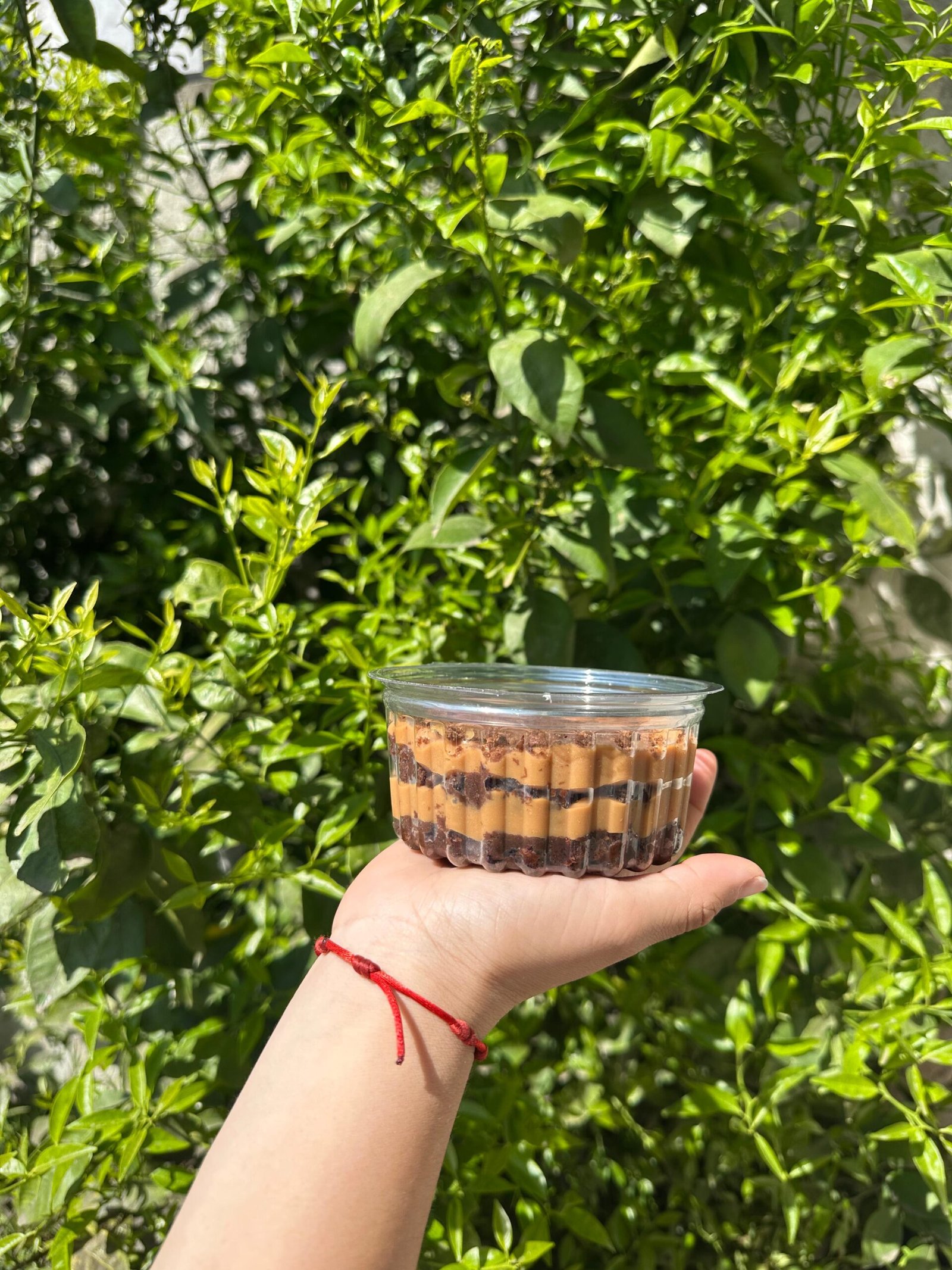 Chocotorta artesanal en vaso con capas de crema y galletitas de chocolate, decorada con una galletita Oreo, sostenida con la mano sobre un fondo natural.